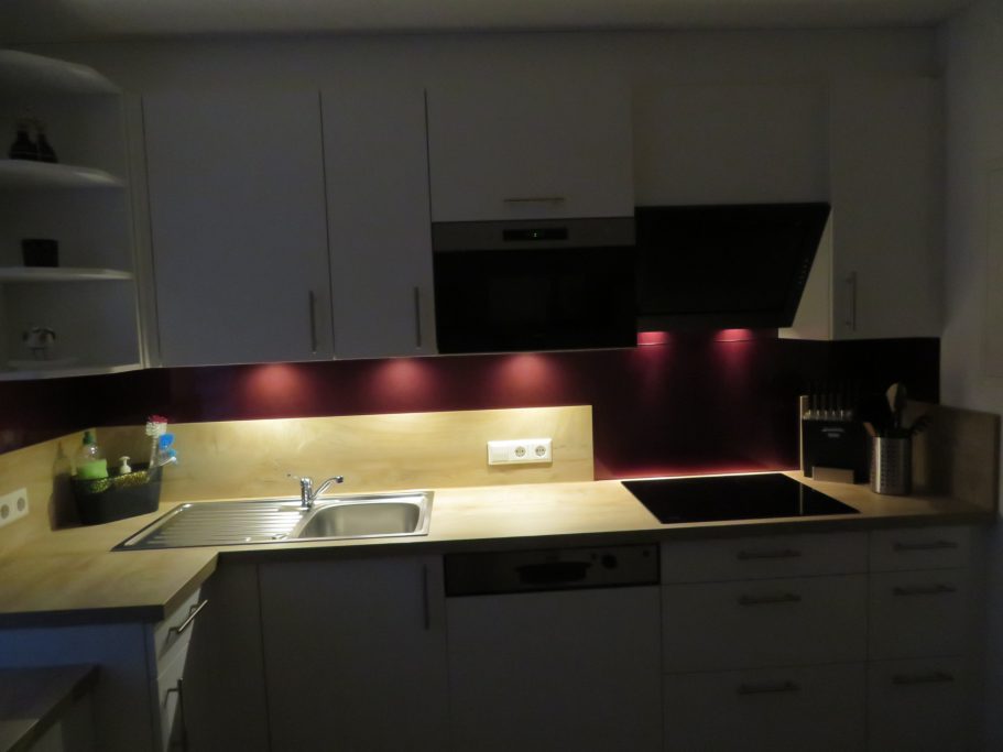 Küche Moderne Küche mit weißen Schränken, Beleuchtung und einem Herd in dunklem Ambiente.