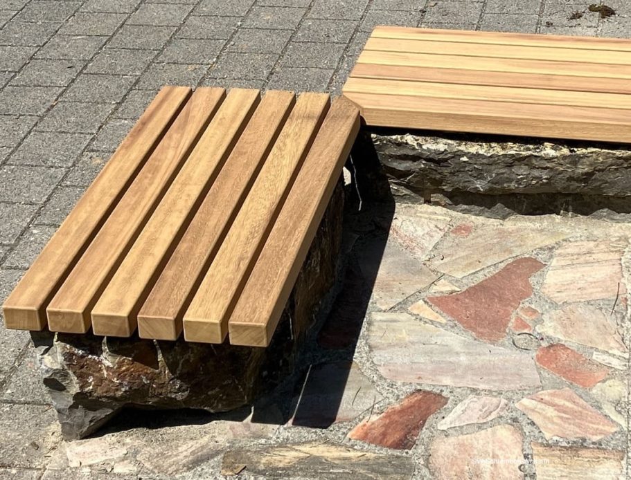 Holzbank Zwei Holzbänke mit steinernen Unterlagen auf einem gepflasterten Boden.